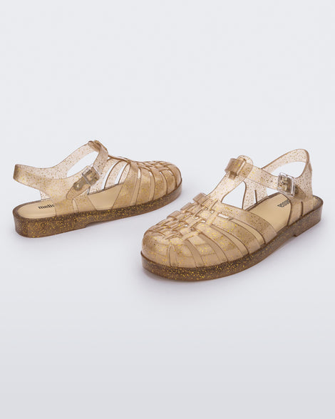 An angled front and side view of a pair of beige glitter Melissa Possession Shiny sandals with several straps, a closed toe front and an ankle strap.