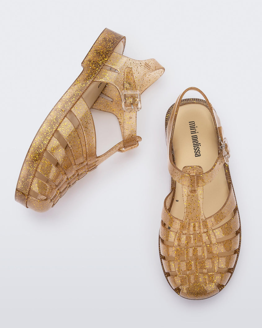 A top and side view of a pair of Beige/Glitter/Gold Mini Melissa Possession Shiny sandals with several straps and a gold glitter base.