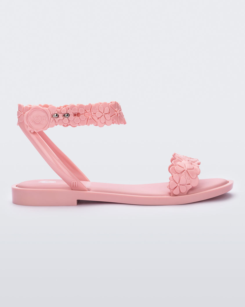 Side view of a Melissa Wave Blossom sandal in pink with floral design ankle and front straps and double snap closure 