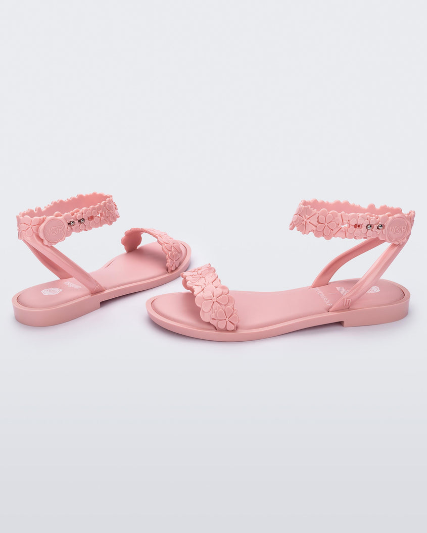Angled view of a pair of Melissa Wave Blossom sandals in pink with floral design ankle and front straps and double snap closure 