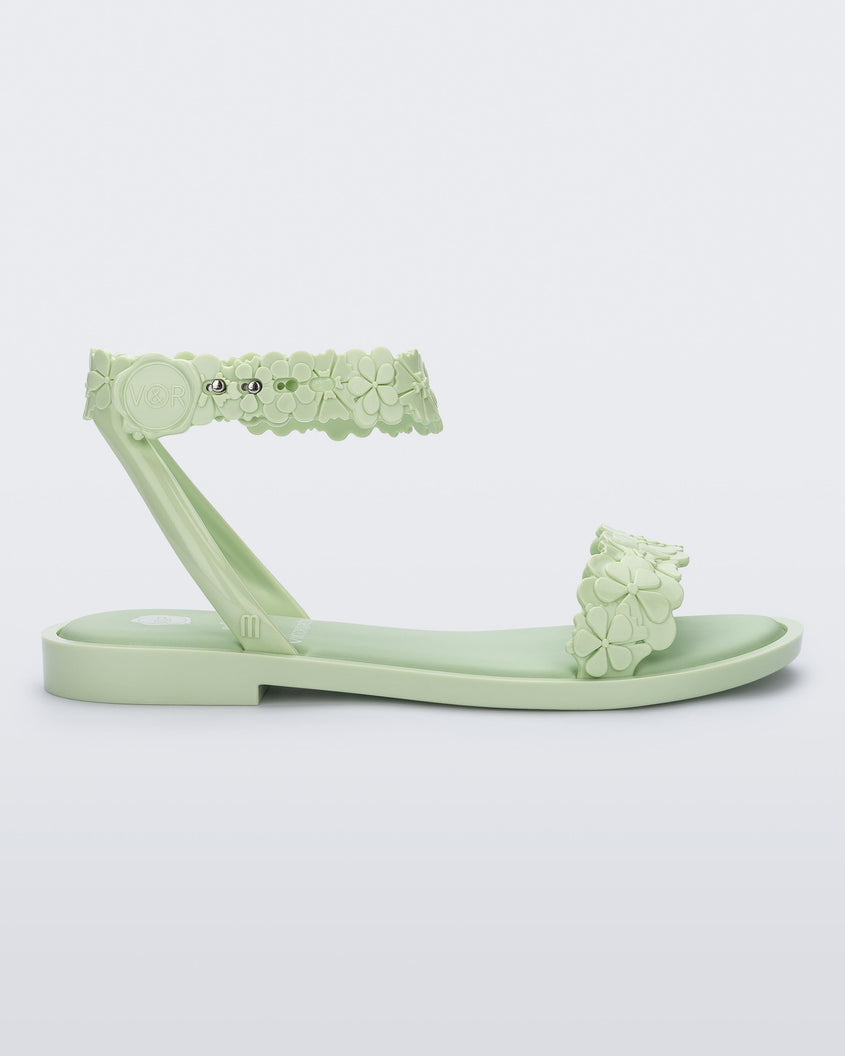 Side view of a Melissa Wave Blossom sandal in Green with floral design ankle and front straps and double snap closure 