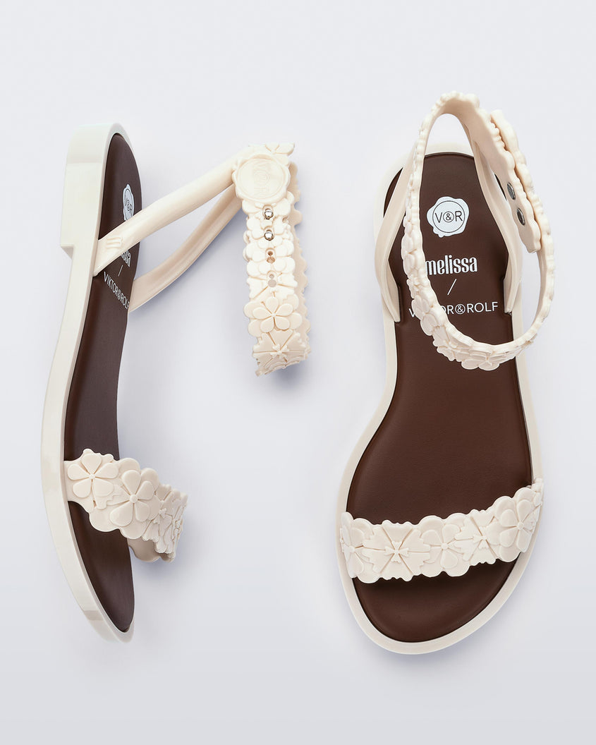 A top and side view of a pair of beige/brown Melissa Wave Blossom Sandals with a floral detail front and ankle strap.