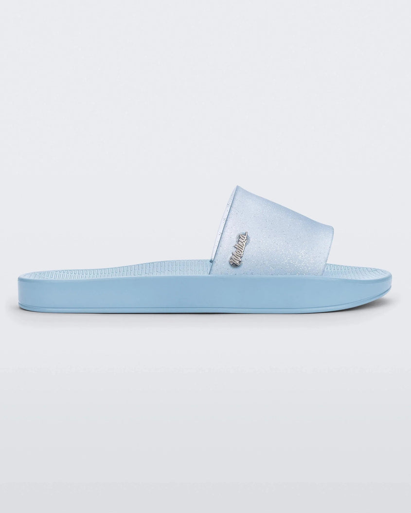 Side view of a blue/clear glitter Melissa Sun Sunset slide with a blue sole and clear blue glitter front strap.