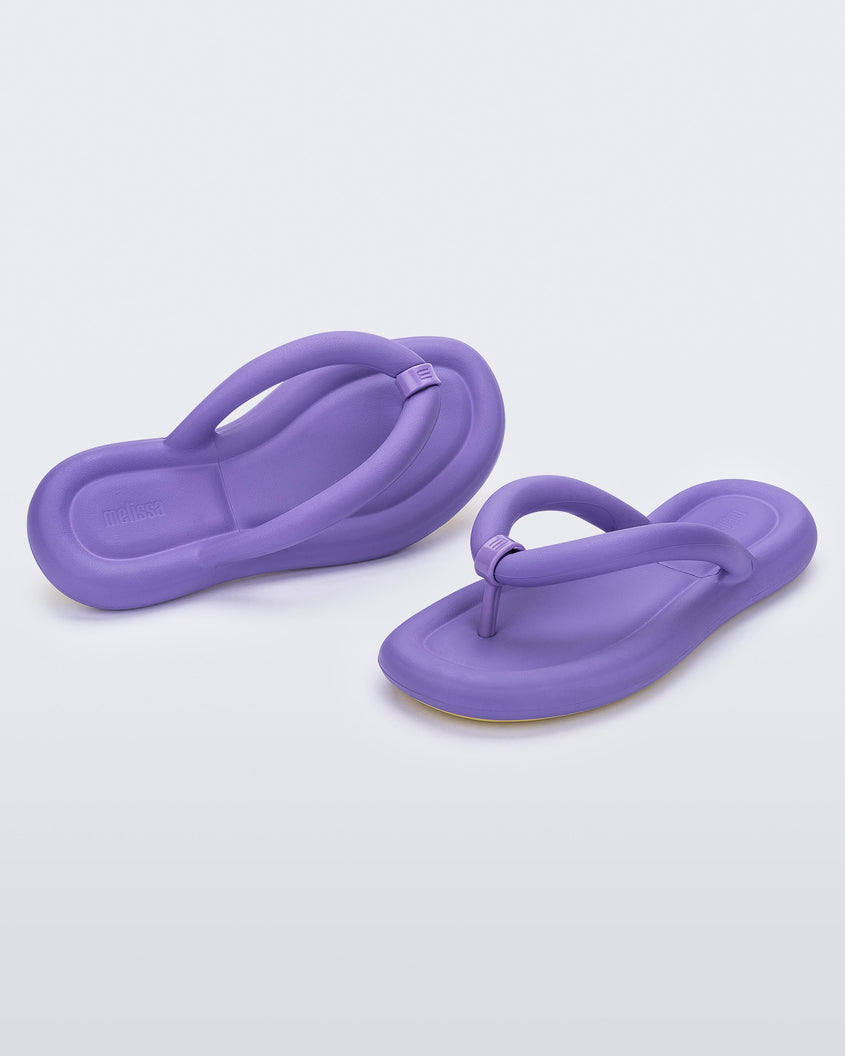 An angled front and side view of a pair of lilac Melissa Free Flip Flops with puffer-like straps.