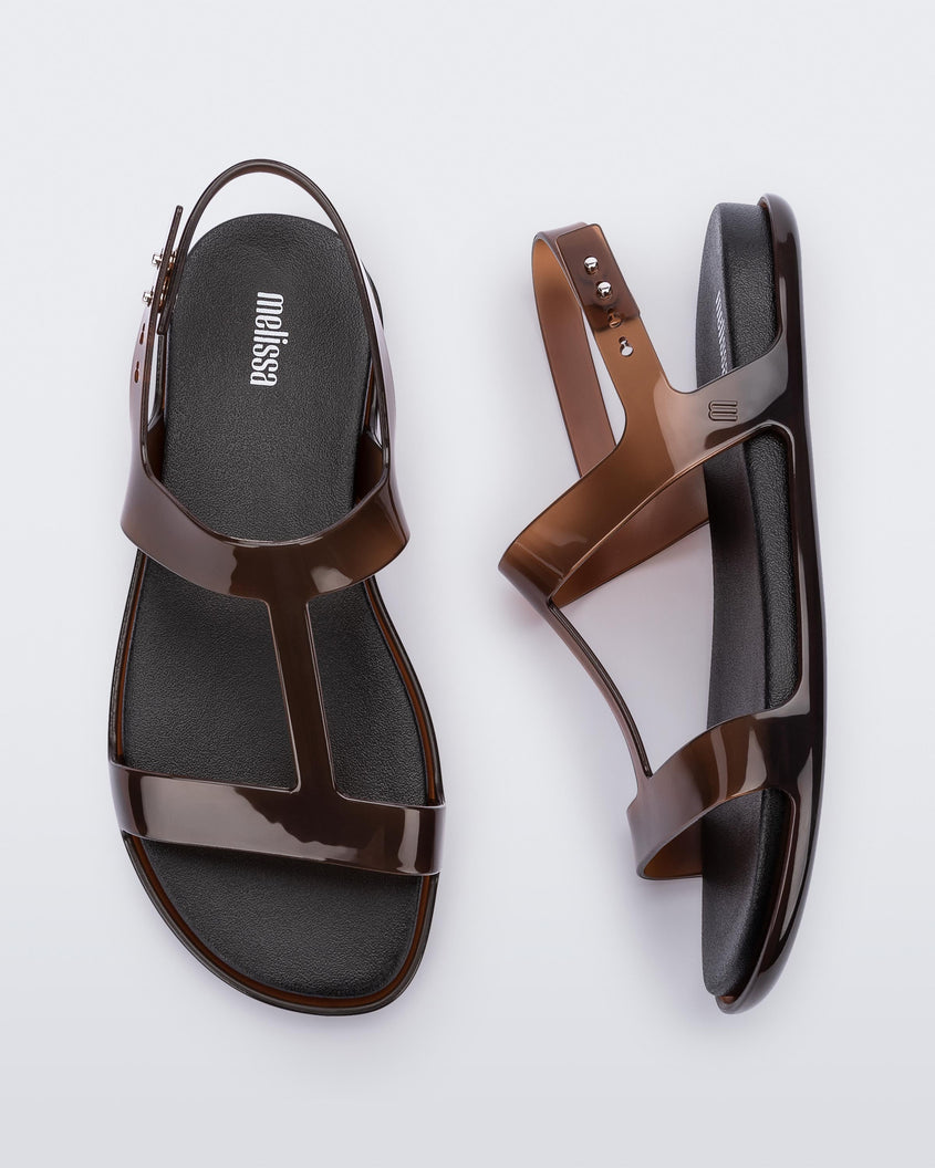 A top and side view of a pair of clear brown / black Melissa Adore sandals with two translucent brown straps, joined together by a third strap and a black insole.
