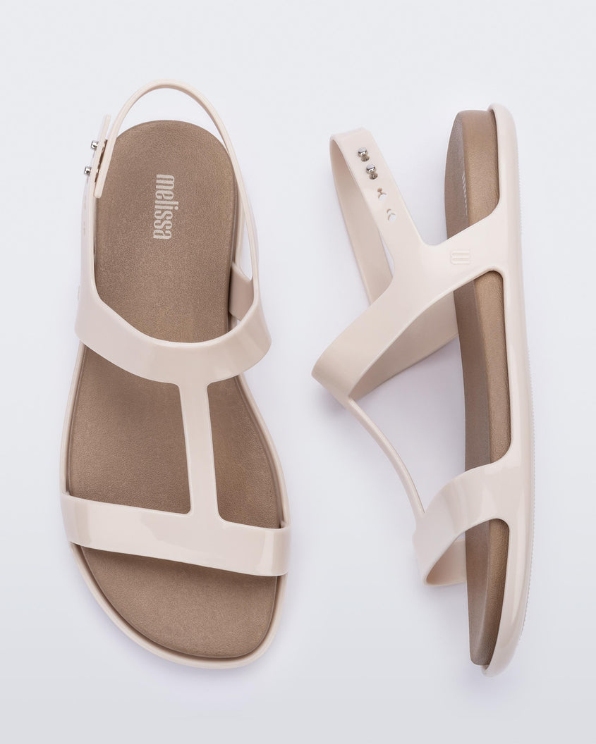 A top and side view of a pair of beige / brown Melissa Adore sandals with two beige straps, joined together by a third strap and a brown insole.