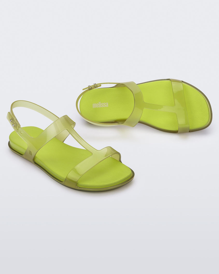 An angled top and side view of a pair of clear green / green Melissa Adore sandals with two translucent green straps, joined together by a third strap and a light green insole.