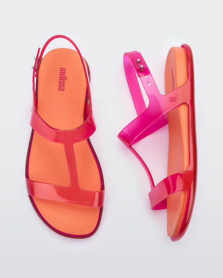 A top and side view of a pair of pink / orange Melissa Adore sandals with two translucent pink straps, joined together by a third strap and an orange insole.