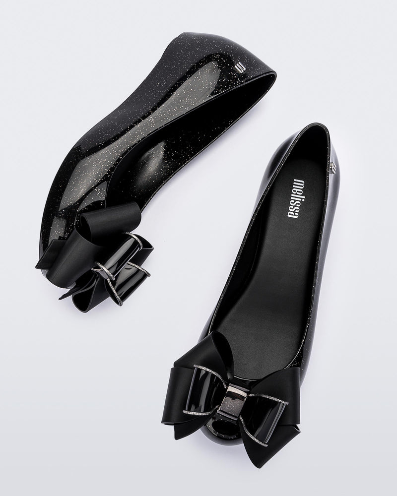 Top and side view of the Melissa Ultragirl ballet flats in black glitter. There is a silver M  located on the back heel. The front toe of the flat has a 3D Bow applique