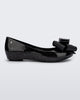 Side view of the Melissa Ultragirl ballet flat in black glitter. There is a silver M  located on the back heel. The front toe of the flat has a 3D Bow applique