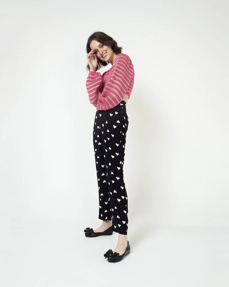 Model posing in a pair of the Melissa Ultragirl ballet flat in black glitter colorway. The model is also wearing black and white heart printed paints and a pink and tan stripped sweater. 