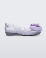 Side view of a Clear Glitter/Lilac Mini Melissa Ultragirl Sweet flat with a clear glitter base and a lilac bow detail on the toe.