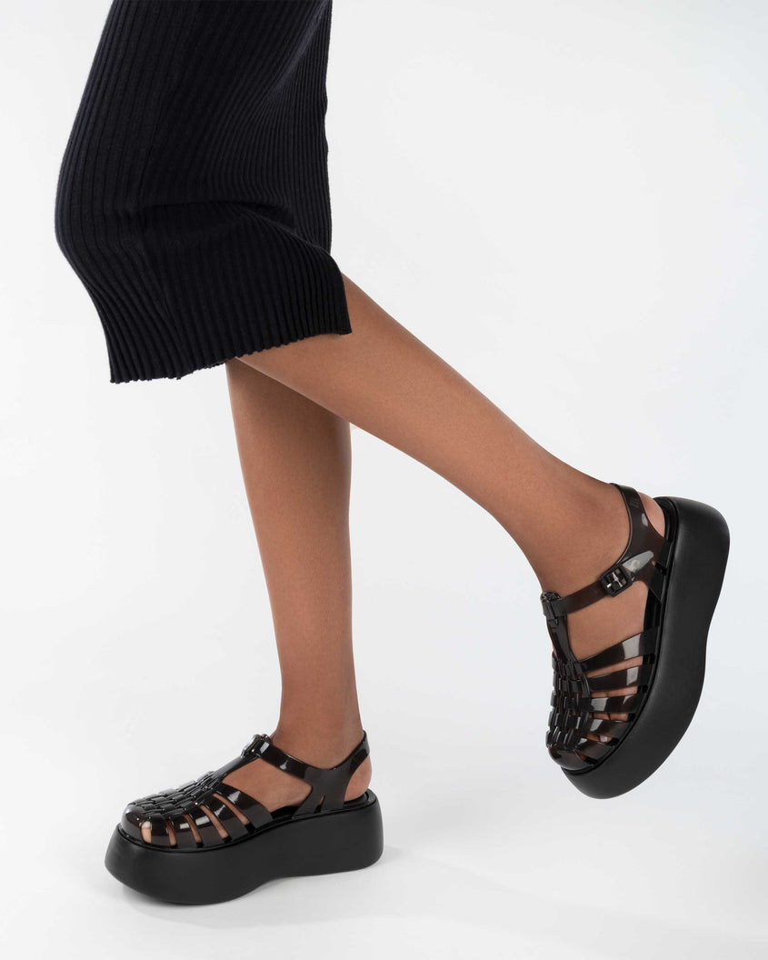 A model's legs in a black skirt and a pair of black Melissa Possession Platform sandals with several straps and a closed toe front.