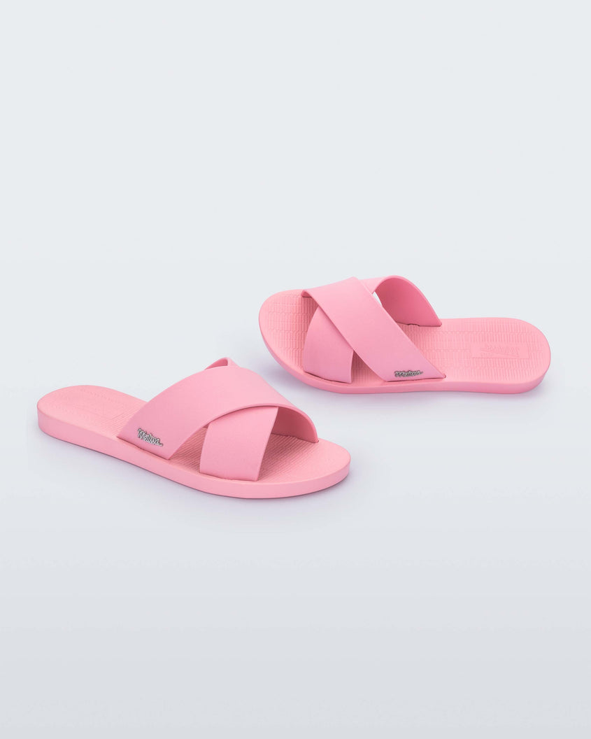 A side and top view of a pair of pink Melissa Sun City Walk slides with a melissa logo on the side and two overlapping straps.