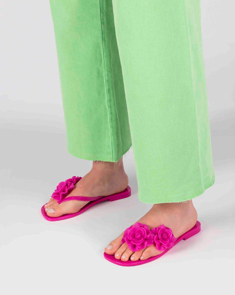 A model's legs wearing green pants and a pair of pink Melissa Harmomic Squared Garden flip flops with flowers on the straps.