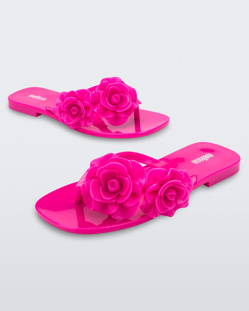 Angled view of a pair of pink Melissa Harmomic Squared Garden flip flops with flowers on the straps.