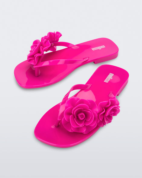 An angled front view of a pair of pink Melissa Harmomic Squared Garden flip flops with flowers on the straps.