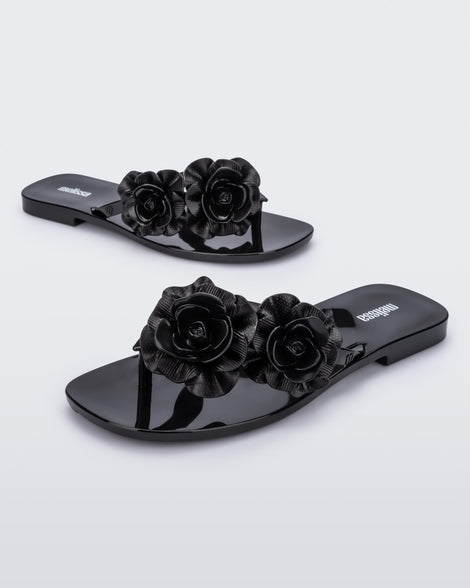 An angled side and front view of a pair of black Harmomic Squared Garden flip flops with flowers on the straps.