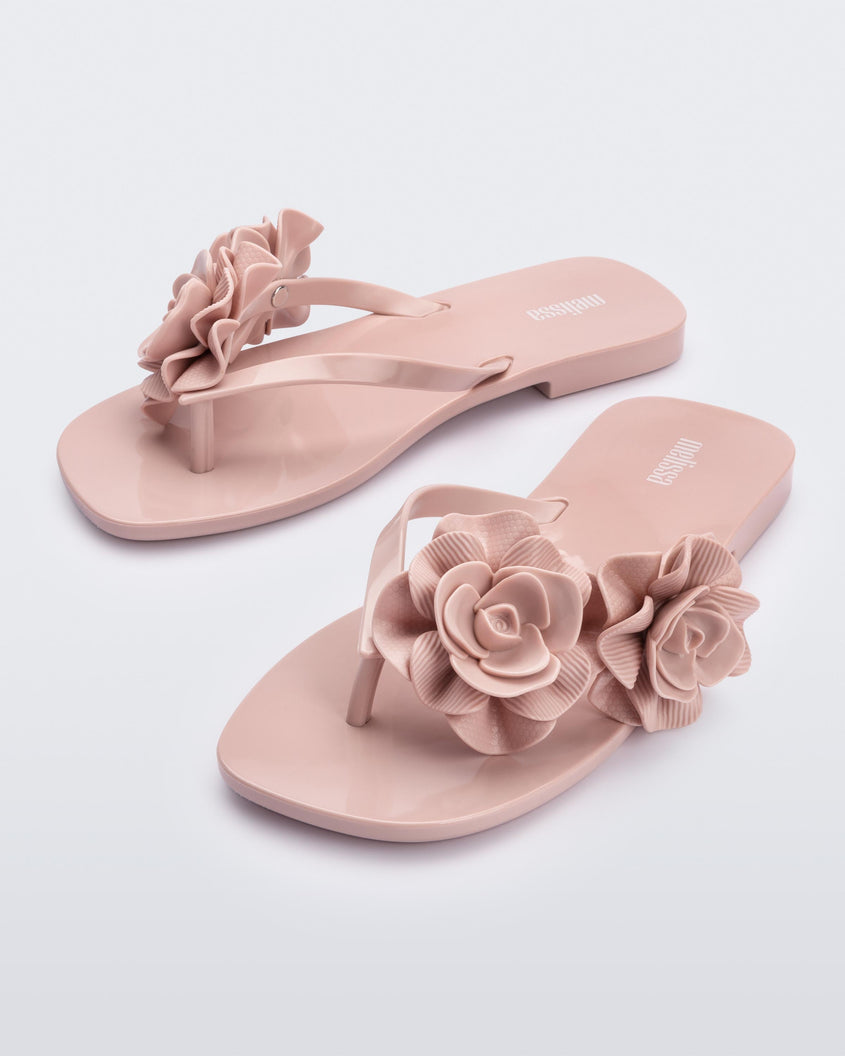 An angled front view of a pair of light pink Melissa Harmomic Squared Garden flip flops with flowers on the straps.
