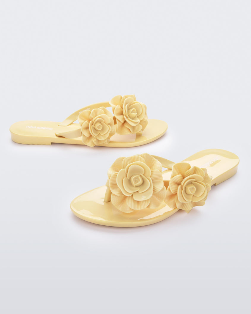 An angled front and side view of a pair of yellow Melissa Harmomic Squared Garden flip flops with flowers on the straps.
