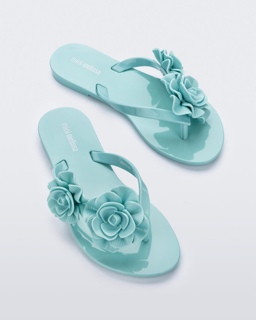 An angled top view of a pair of green Mini Melissa Harmonic Garden flip flops with flowers on the straps.
