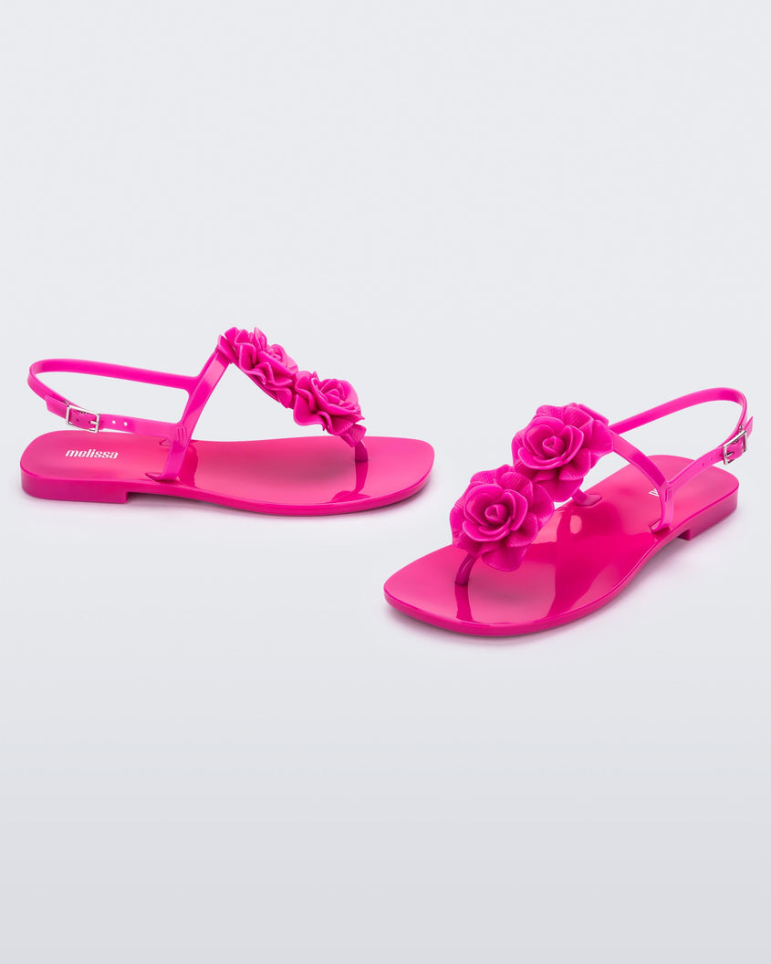 An angled front and side view of a pair of pink Melissa Harmomic Squared Garden flip flops with flowers on the straps.