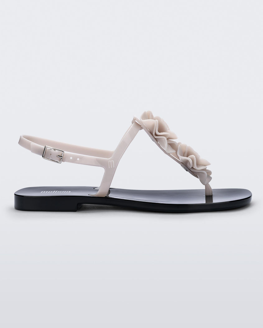 Side view of a beige/black Melissa Harmonic Squared Garden sandal with a beige flower decoration on the front strap and a black sole.