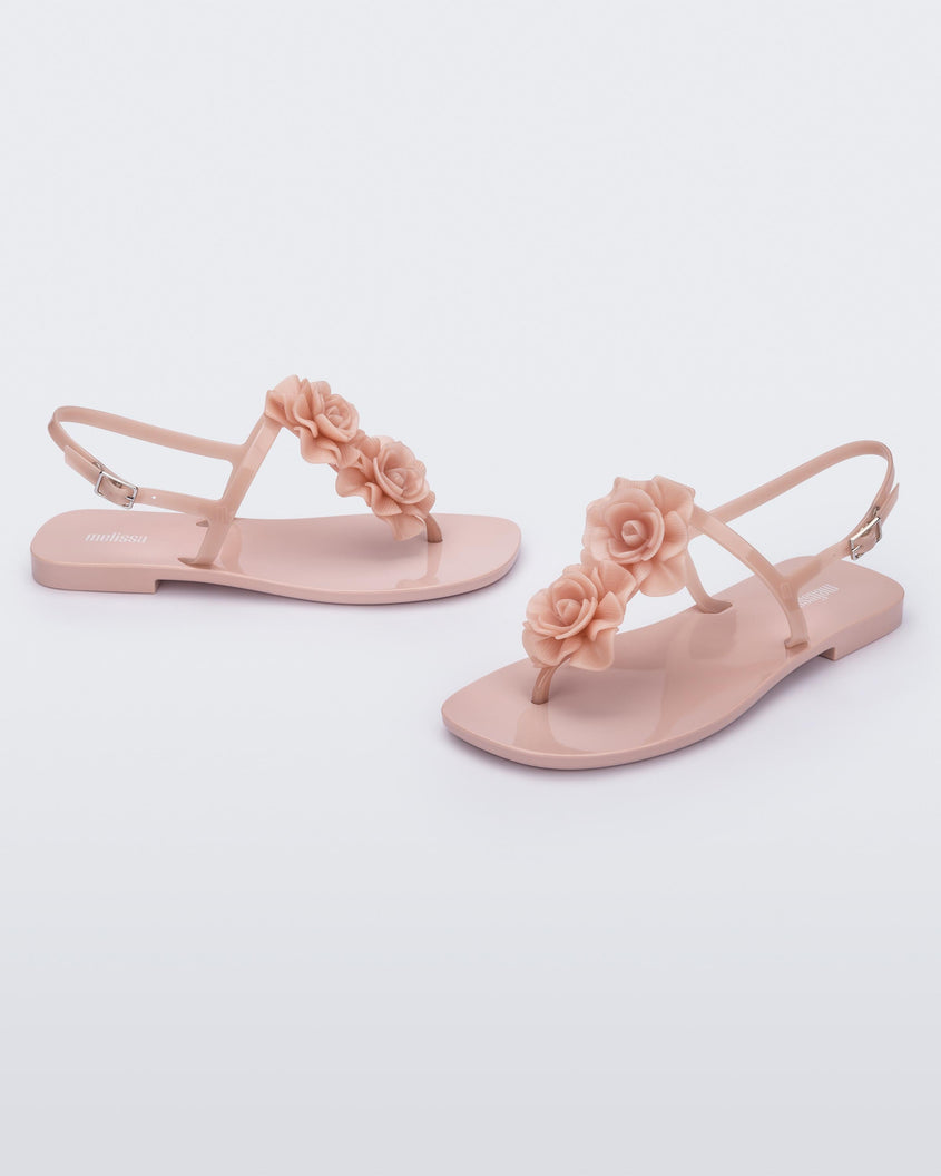 An angled front and side view of a pair of light pink Melissa Harmonic Squared Garden flip flops with flowers on the straps.