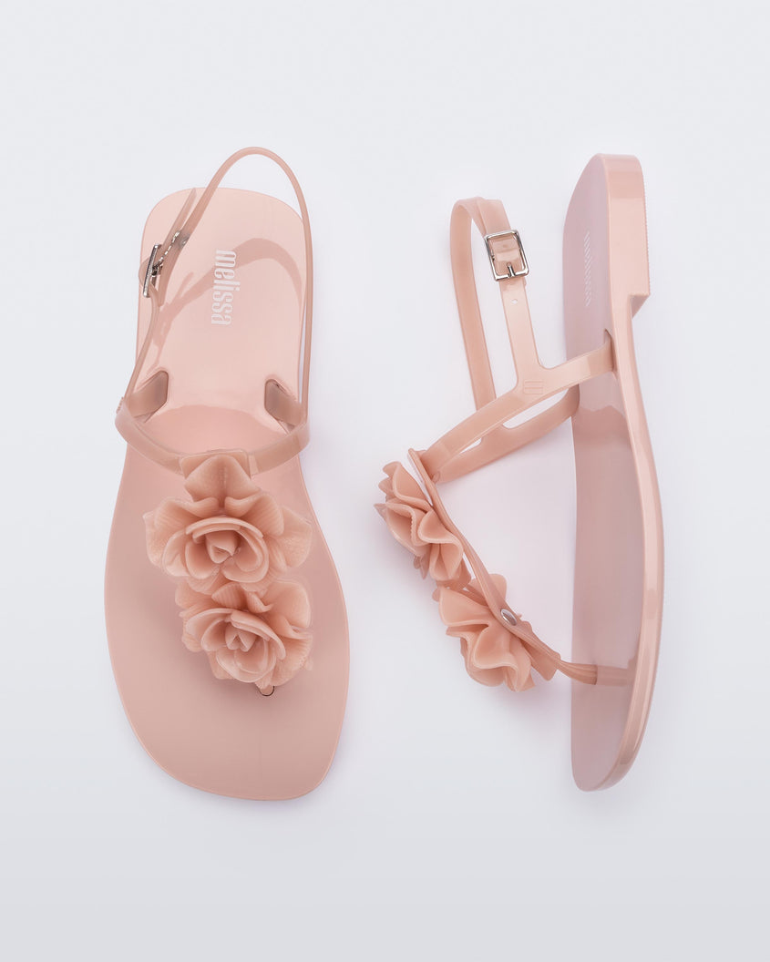 A top and side view of a pair of light pink Melissa Harmonic Squared Garden sandals by Melissa with flower decorations on the front straps.