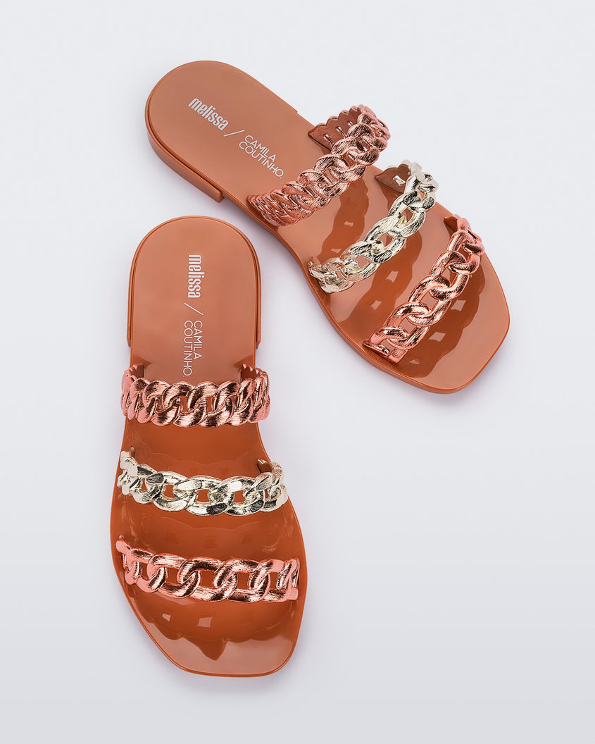 A top view of a pair of orange Melissa Feel slides three gold and orange chain detail straps.
