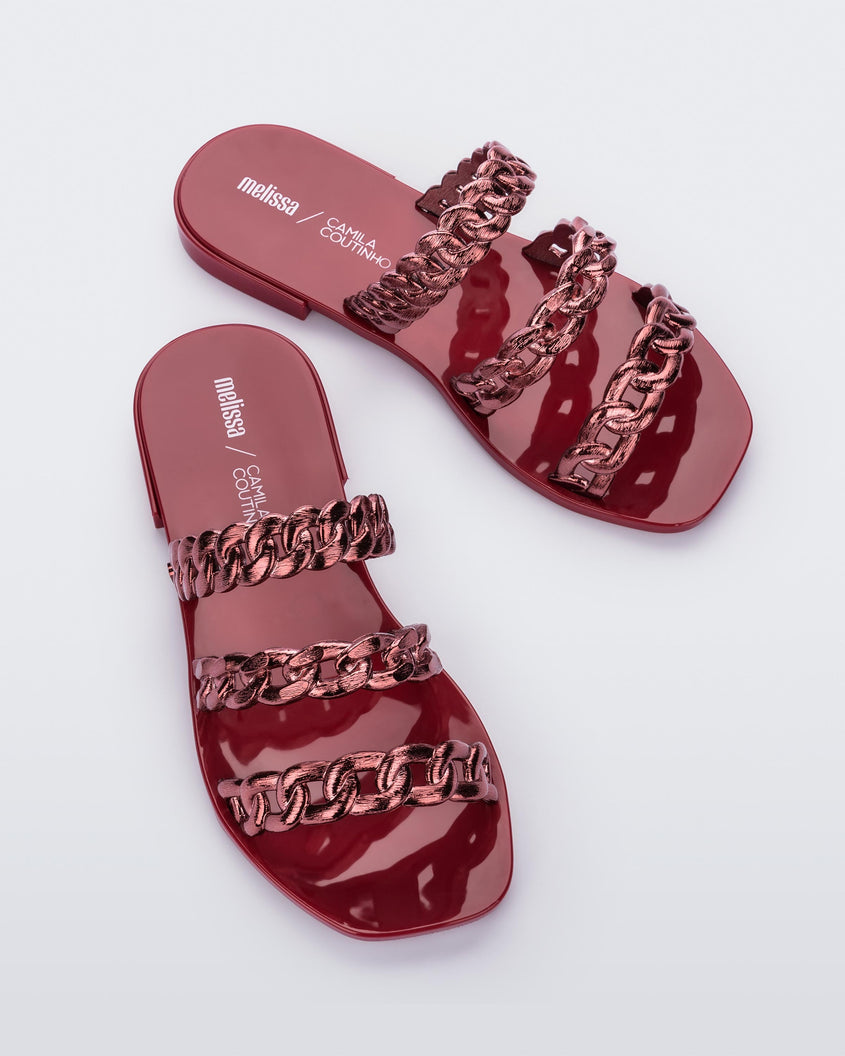 A top view of a pair of red Melissa Feel slides with three chain detail straps.