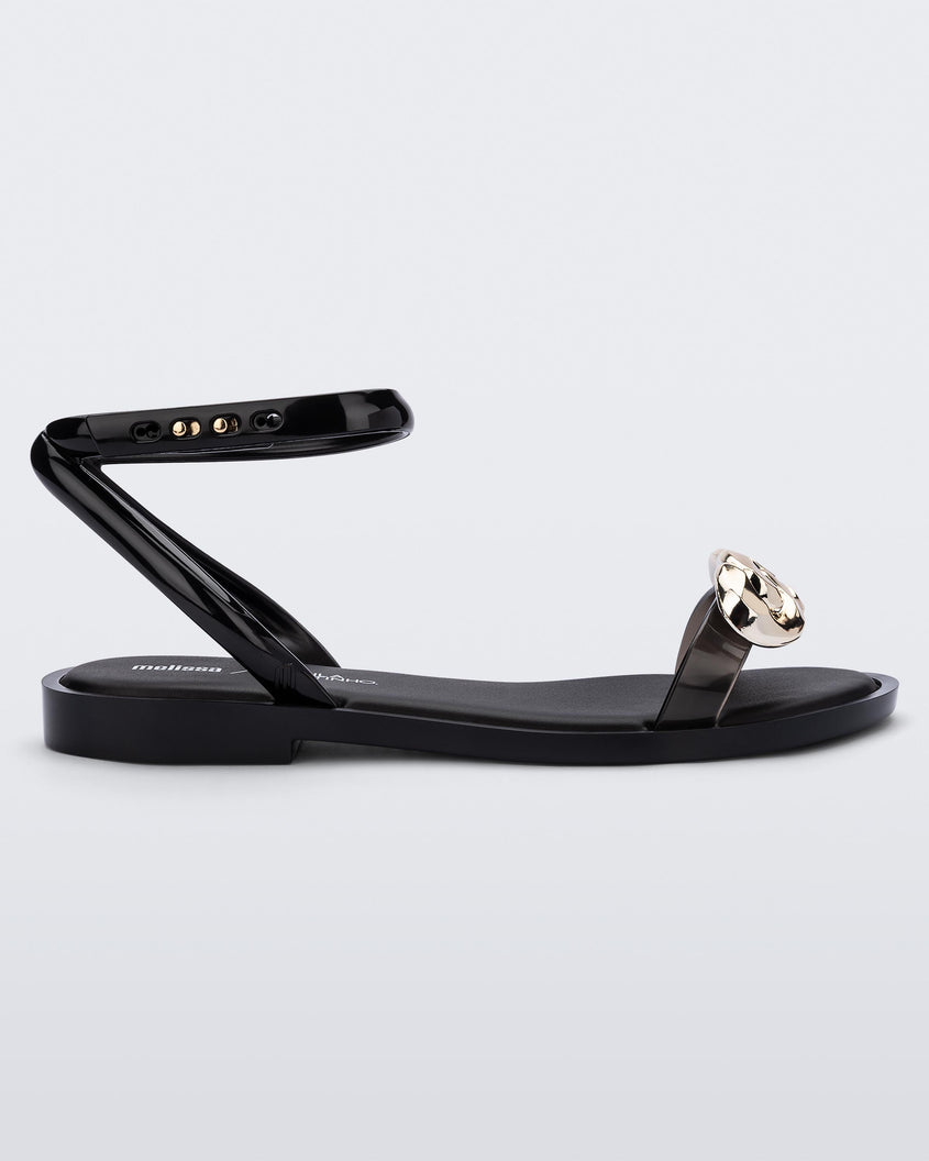 Side view of a black/gold Melissa Dare sandal with a gold metal chain buckle.