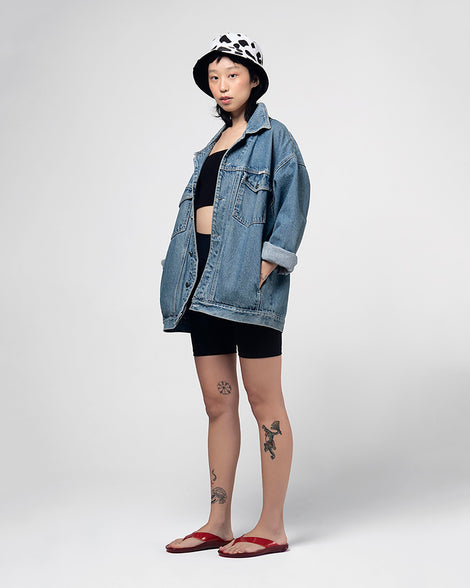A model in a denim jacket, hat, black top and black bottoms, posing for a picture in a pair of clear red Melissa Real Jelly Flip Flops.