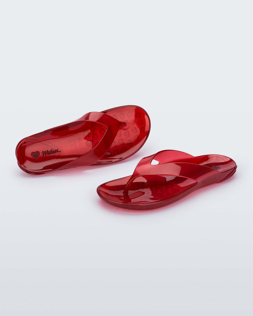 An angled front and top view of a pair of clear red Melissa Real Jelly Flip Flops.