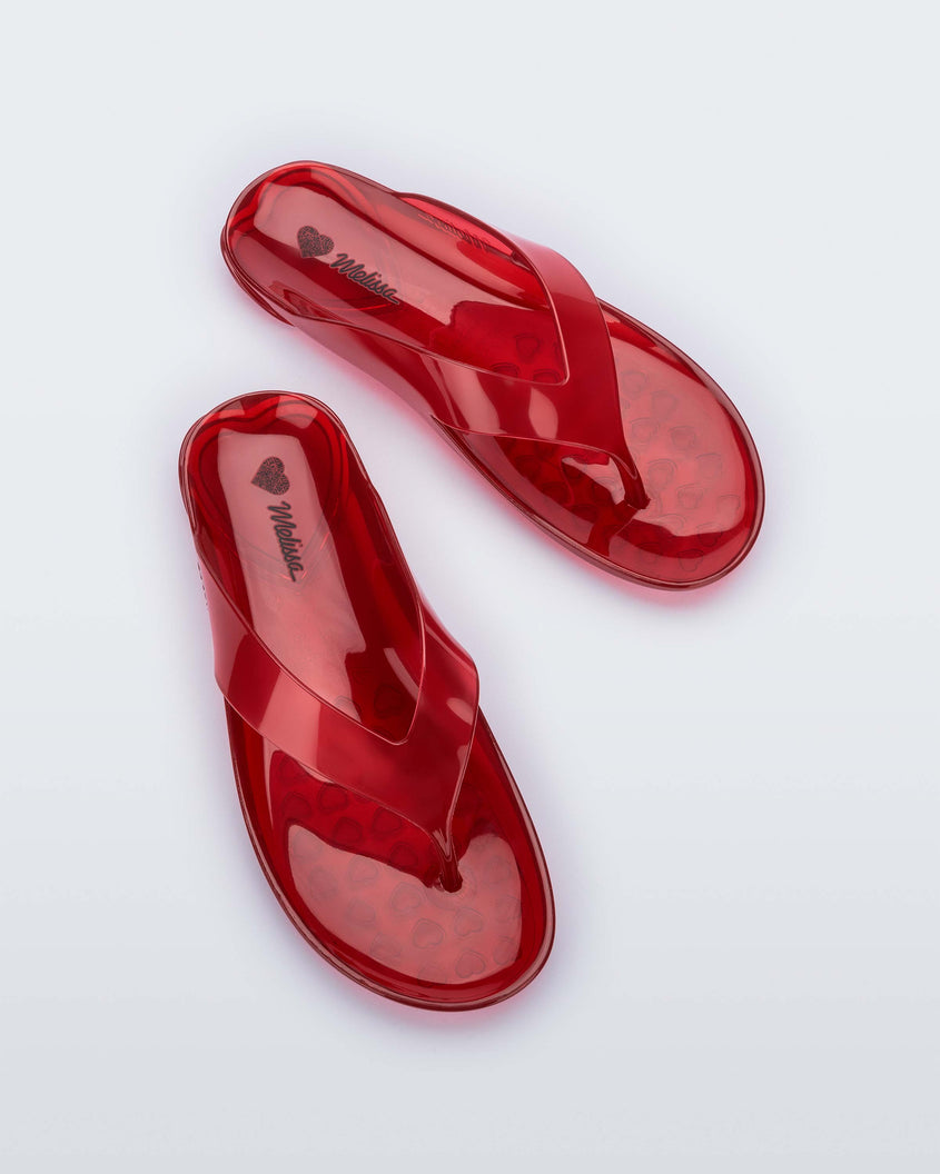 Top view of a pair of clear red Melissa Real Jelly Flip Flops.