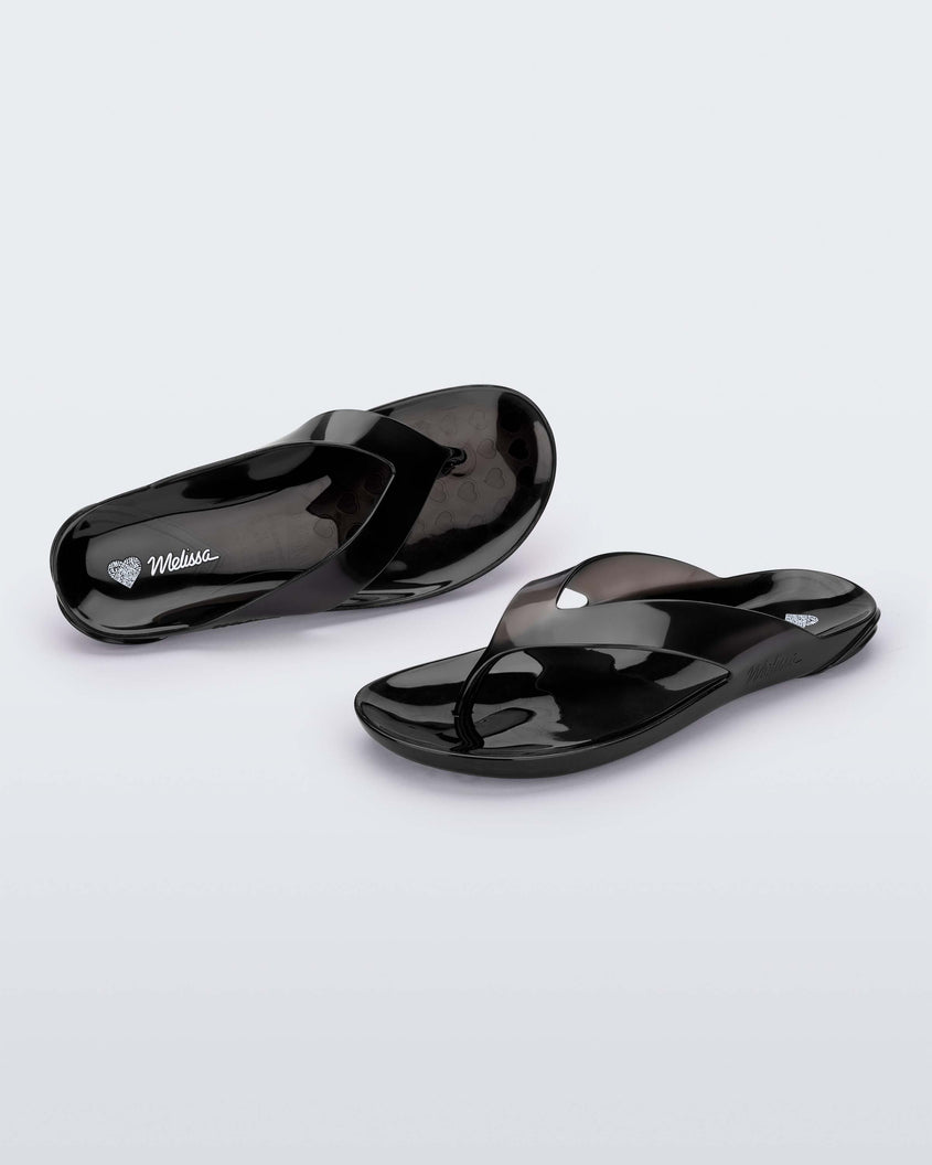 A front and top view of a pair of clear black Melissa Real Jelly Flip Flops.