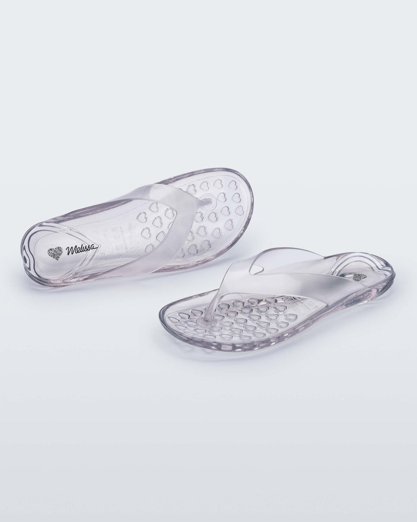 An angled front and top view of a pair of clear Melissa Real Jelly Flip Flops.