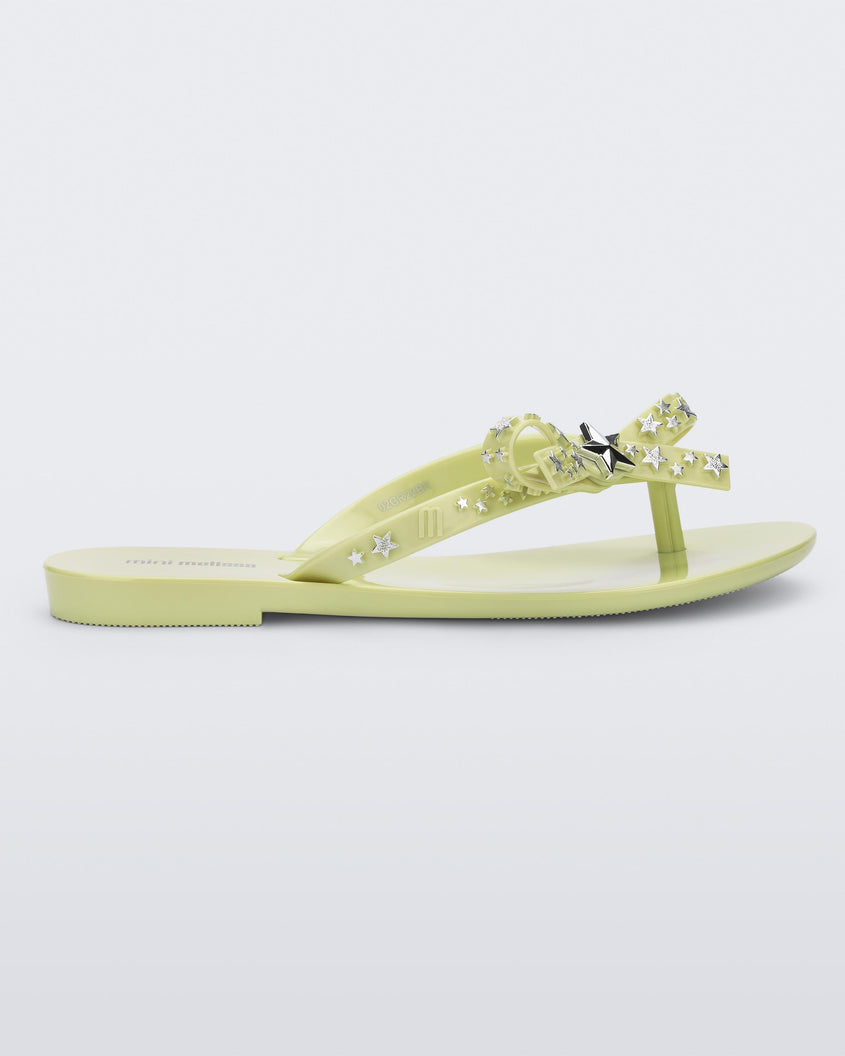Side view of a green Mini Melissa Harmonic Stars flip flop with a bow and silver star details on the straps.