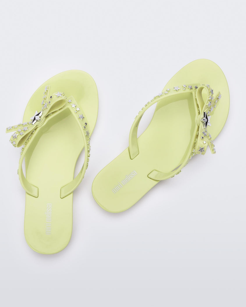 A top back view of a pair of green Mini Melissa Harmonic Stars flip flops with a bow and silver star details on the straps.