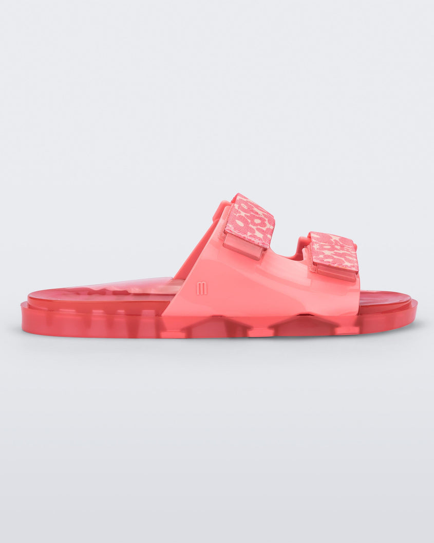 Side view of a pink Melissa Brave Wide slide with a pink base, pink and yellow floral print velcro straps and a translucent pink insole.
