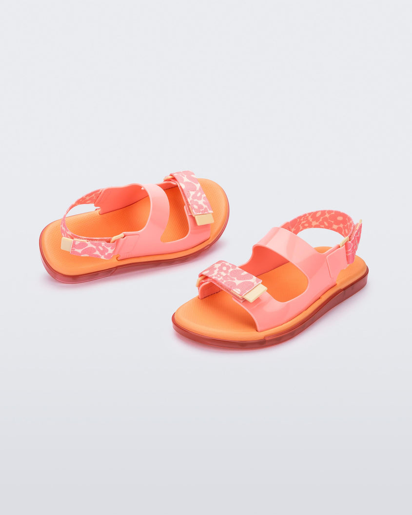 An angled top and side view of a pair of pink Melissa Brave Papete sandals with an orange insole, pink flower print, pink straps and a velcro back.