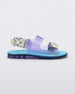 Side view of a lilac Melissa Brave Papete sandals with a blue insole, purple and green flower print and transparent lilac straps and a velcro back.