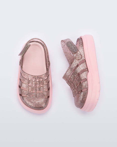A top and side view of a pair of pink/glitter Mini Melissa Sunday sandals with a glitter base, closed toe front and pink sole.