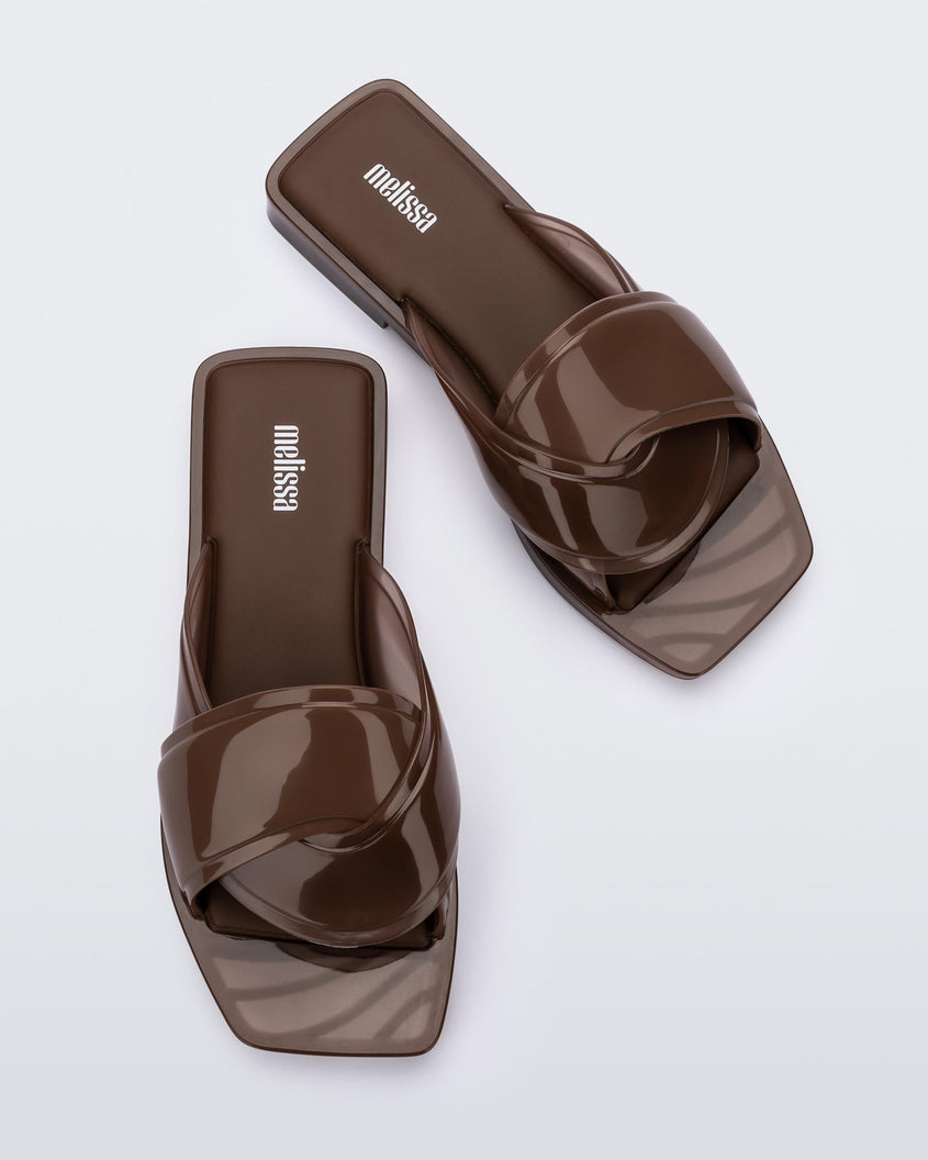 Top view of a pair of brown Melissa Brigitte slides with a weft designed upper strap.