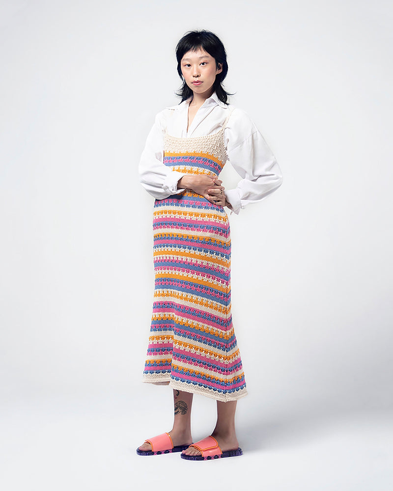 A model posing for a picture in a white top, colorful dress and a pair of lilac/pink Melissa Brave Slides with a pink and orange velcro top strap and translucent lilac insole.
