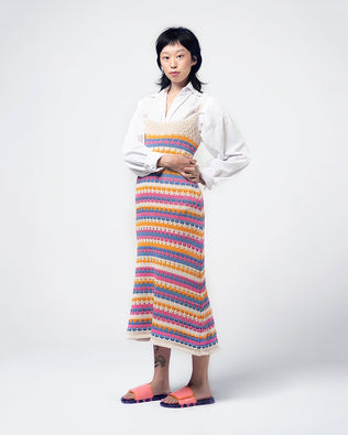 A model posing for a picture in a white top, colorful dress and a pair of lilac/pink Melissa Brave Slides with a pink and orange velcro top strap and translucent lilac insole.