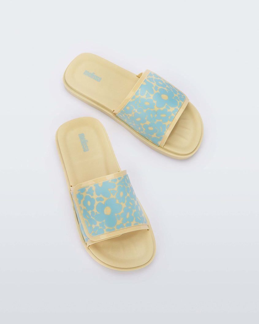 Top view of a pair of yellow/blue Melissa Brave Slides with a yellow and blue floral patterned velcro top strap and yellow insole.