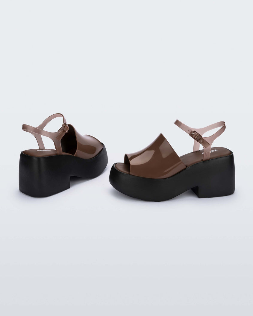 A side and back view of a pair of black/brown Melissa Pose platform sandals with a brown front strap, a clear brown ankle strap and a black sole.