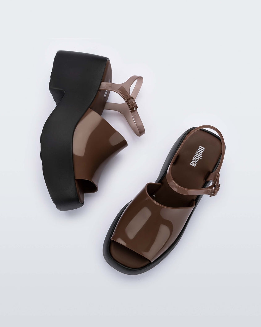 A top and side view of a pair of black/brown Melissa Pose platform sandals with a brown front strap, a clear brown ankle strap and a black sole.