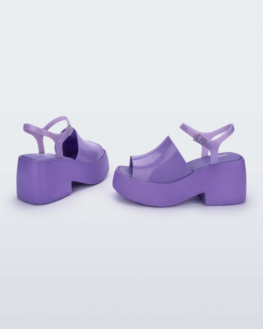 A side and back view of a pair of lilac Melissa Pose platform sandals with a lilac front strap, a clear lilac ankle strap and a lilac sole.
